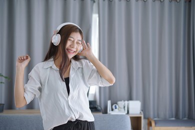 happy asian carefree young woman dancing alone having fun at home listening to good music.