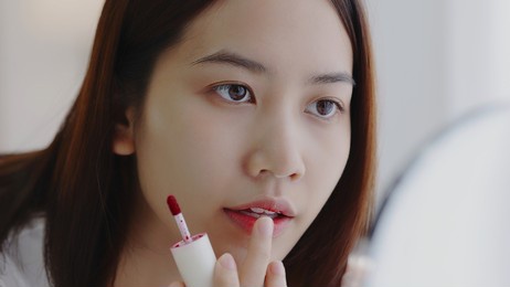 beautiful asian girl looking at mirror, applying lip on her lips.