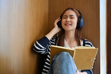 relaxed and happy young asian female college student enjoy listening to music on her wireless headphones in the library.