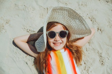 a little blonde girl in a straw hat lies on a sandy beach. girl sunbathing on the sand