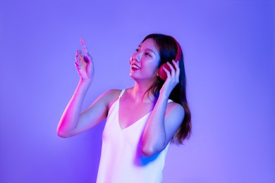 young asian woman long hair wearing headphones finger pointing on purple screen background.