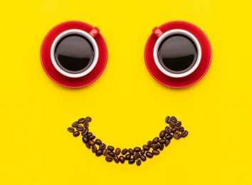 two cup of coffee and coffee beans with smile face concept, top view on yellow background. for morning happy concept 