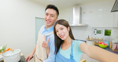 point of view healthy asian young couple wearing apron are cooking and they taking selfie through mobile phone in light white interior style kitchen at home