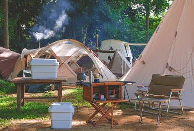 outdoor kitchen equipment and wooden table set with field tents group in camping area of natural parkland at morning time