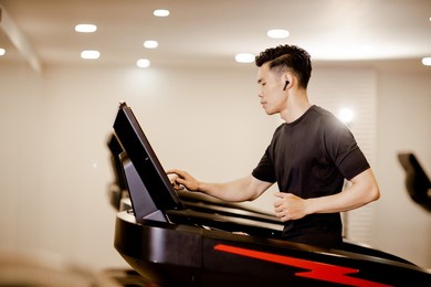asian young man in sportswear running on machine treadmill at fitness gym. concept for exercising, fitness, and healthy lifestyle.