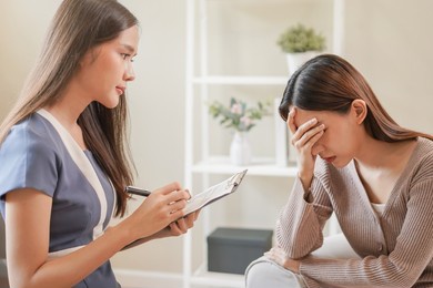 psychology, depression. sad, suffering asian young woman consulting with psychologist, psychiatrist while patient counseling mental with doctor woman taking notes at clinic. encouraging, therapy.