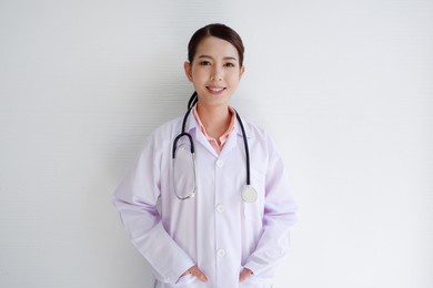 smiling asian female doctor placing stethoscope on her shoulder on white background.