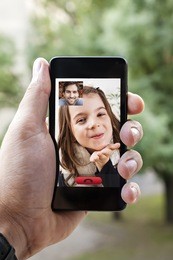 close up of a male hand holding a smart phone during a video call with his daughter