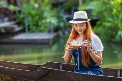 young asian woman tourist is travel with wooden boat in floating market in thailand and having local street food for southeast asia tourism