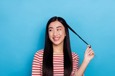 photo of pretty positive vietnamese girl hand touch play hairdo curl look empty space isolated on blue color background