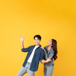 two young good looking asian couple using isolated on yellow background presenting to copy space feeling excited