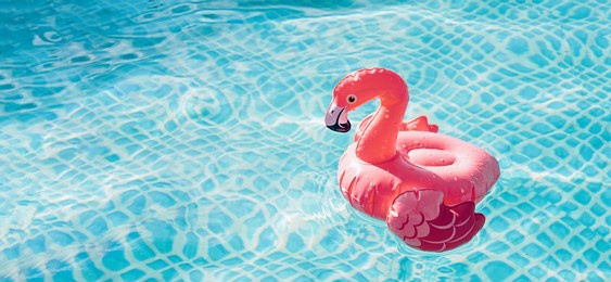 small inflatable flamingo on blue water background, summer concept banner
