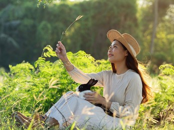 pretty asian woman enjoying the nature sitting with cute little bunny rabbit in the forest.
