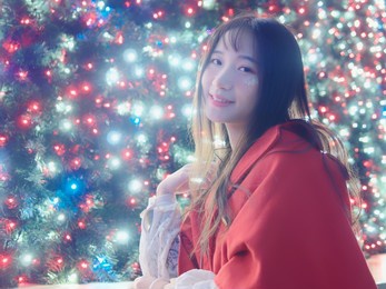 portrait of beautiful chinese girl with black long hair in red christmas clothes sitting and smiling at you with colorful light background, glamour young chinese cheerful stylish woman.