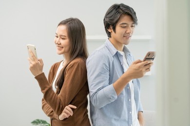 infidelity, suspicion asian young couple love standing back to back, husband watching his wife using mobile phone, spying his girlfriend while woman typing a message, man distrust and jealousy at home