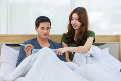 asian happy romantic male female husband and wife lover couple lay down smiling together on pillow under blanket on bed using laptop notebook computer and credit card shopping making payment online.