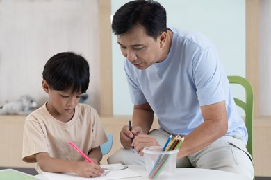 asian little boy drawing on pages with colour pencils on table at classroom. kid learning by drawing. education concept