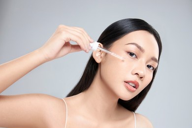 beautiful young asian woman apply facial serum isolated on light grey background. skin care and rejuvenation.