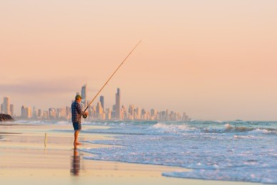 fisherman fishing at sunrise on the gold coast with surfers paradise in the background.