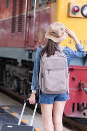 young asian woman traveler with backpack in the railway, backpack and hat at the train station with a traveler, travel concept. woman traveler tourist walking at train station
