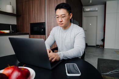 asian man working with laptop while sitting in kitchen at home