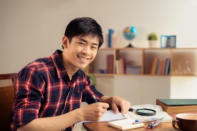 portrait of cheerful asian student doing homework