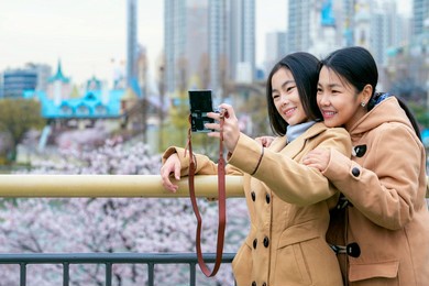 asian woman traveler mother and her daughter take selfie togather at view point in seoul city, south korea in winter season with cherry blossom background