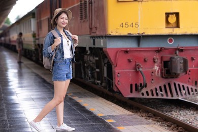 young asian woman traveler with backpack in the railway, backpack and hat at the train station with a traveler, travel concept. woman traveler tourist walking at train station