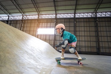 asian child or kid girl playing skateboard or riding surf skate up to wave ramp or wave bank to fun bottom turn in indoor skate park by extreme sports to wearing helmet knee support for body safety