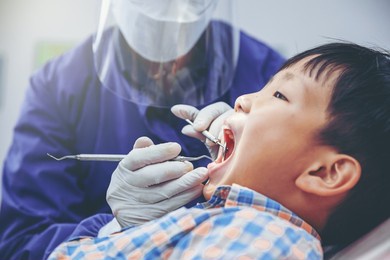 dentist examines child's teeth using metal instruments at dental clinic. dentistry and healthcare concept