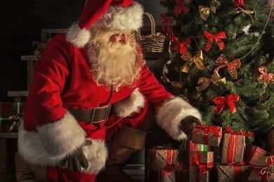 santa claus brought gifts for christmas. santa is placing gift boxes under christmas tree