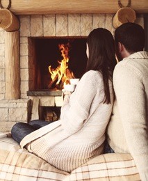 couple holding cups with hot chocolate with marshmallows in front of lit fireplace
