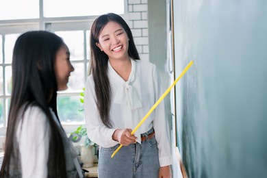 smiling asian teacher woman teaching student in english classroom, female teacher writing on blackboard, high school and back to school concept.