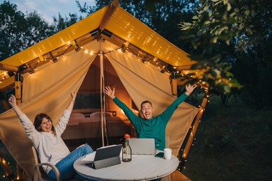 happy family couple freelancers working laptop on a cozy glamping tent in summer evening. luxury camping tent for outdoor holiday and vacation. lifestyle concept