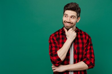 young happy smiling fun cool man he 20s wear red shirt grey t-shirt look aside on workspace area mock up prop up chin isolated on plain dark green background studio portrait people lifestyle concept
