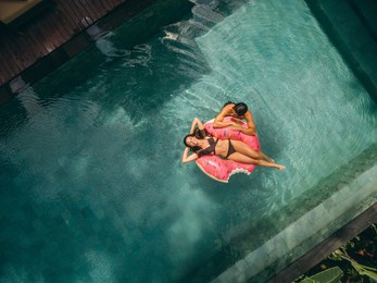 aerial view of young woman and woman relaxing on inflatable ring in resort pool. couple enjoying holidays at luxury resort.