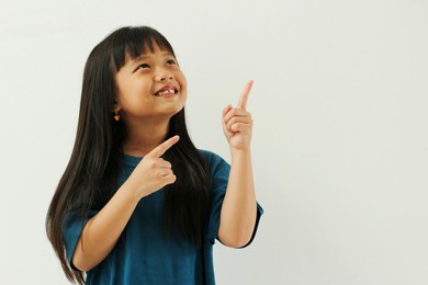 lose-up portrait of asian girl long straight black hair nice cute attractive smiling cheerful pointing two fingers looking up copy space isolated white background