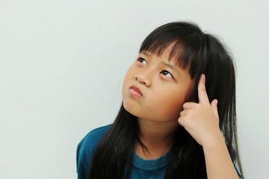 portrait of asian girl with straight black hair touching her head and expressing confusion thinking imagining dreaming good idea looking up isolated on white background. close up copy space.