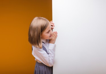 a smiling schoolgirl stands behind a white blank panel highlighted on a yellow background. an empty space for text looks out from behind the banner.