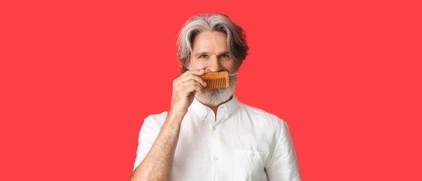 stylish senior man with hair comb on red background with space for text