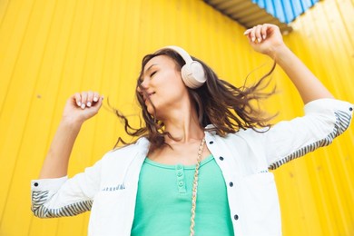 a full-length view of a beautiful cheerful girl jumping while listening to a melody isolated against a bright yellow background. a young woman with headphones dancing on the street . generation z