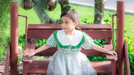 positive charming 4 years old cute baby asian girl, little preschooler child sitting on swing chair and looking to the left.