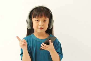 portrait of asian girl with black hair isolated on white background looking at camera with headphones in ear while holding cellphone