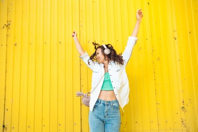 a full-length view of a beautiful cheerful girl jumping while listening to a melody isolated against a bright yellow background. a young woman with headphones dancing on the street . generation z