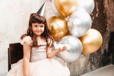 a happy little girl makes a wish and blows out the candles on the cake. balloons. space for text. decorative wall.birthday
