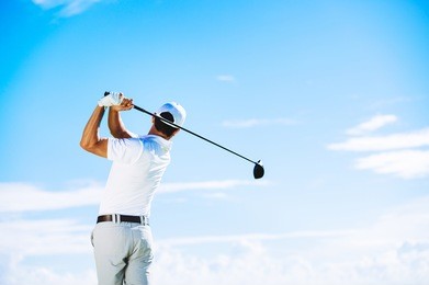 man swinging golf club with blue sky background