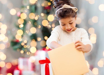 holidays, presents, childhood and people concept - smiling little girl with gift box over living room and christmas thee background
