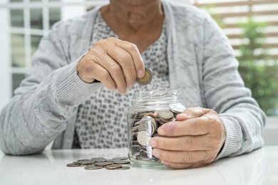 asian senior or elderly old lady woman holding counting coin money in glass jar. poverty, saving problem in retirement.