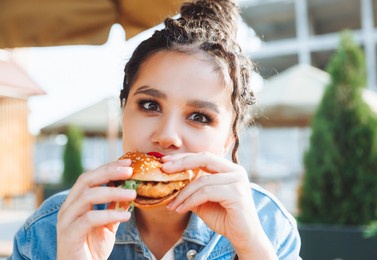 a young glamorous woman with dreadlocks and red lipstick is sitting and eating a burger in a street cafe, the concept of eating. long-lasting lipstick