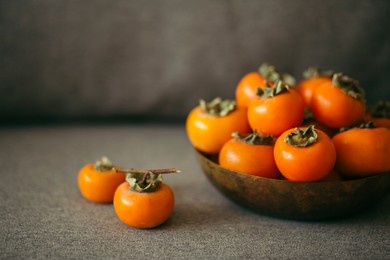 fresh orange organic ripe fuyu persimmons fruits in a cooper bowl with a grey background. copy space for text and content.thanksgiving table in autumn.